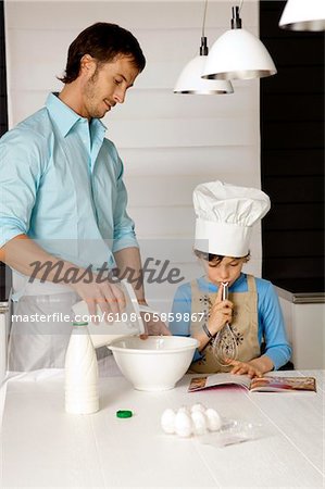 Mid adult man making a cake with his son in the kitchen