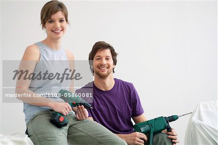 Portrait of a mid adult man and a young woman holding drills
