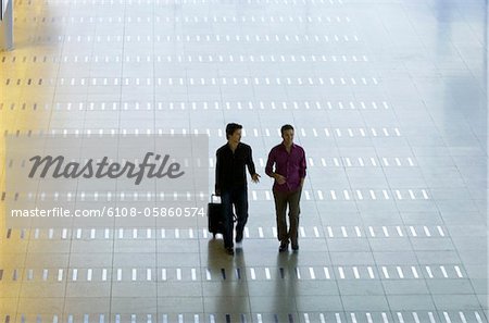 High angle view of a mid adult man walking with a young man at an airport lobby