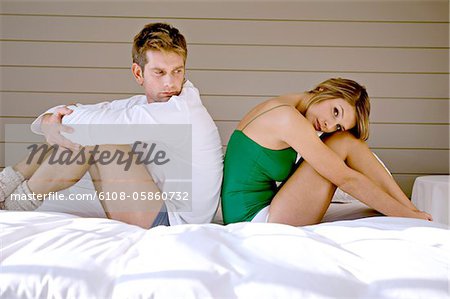 Side profile of a mid adult man and a young woman sitting back to back on the bed