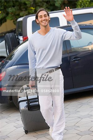 Man pulling luggage and waving hand