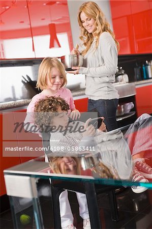 Boy playing a video game with his sister and mother in the background