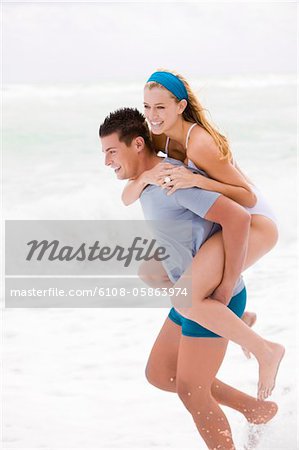 Man giving woman piggyback ride on the beach