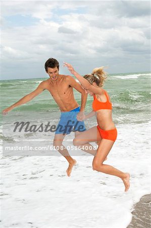 Couple holding hands and jumping on the beach