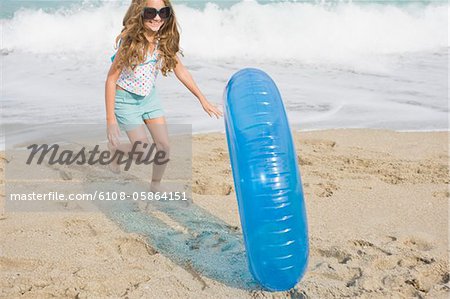 Girl rolling an inflatable ring on the beach