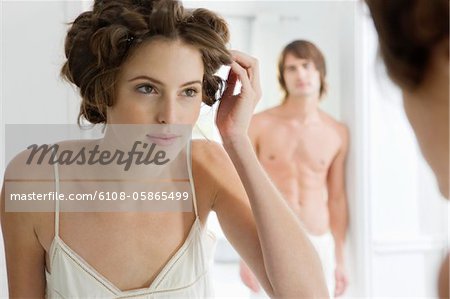 Woman using curlers with her boyfriend in the background