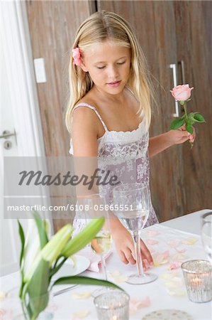 Girl holding a flower and standing at a dining table