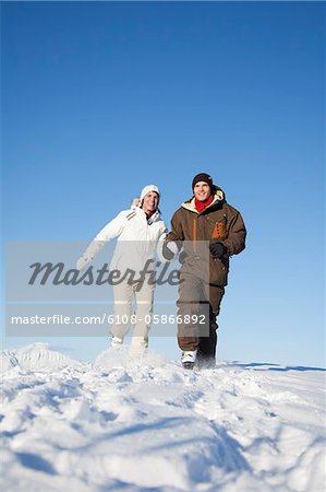 Young couple holding hands, running in snow