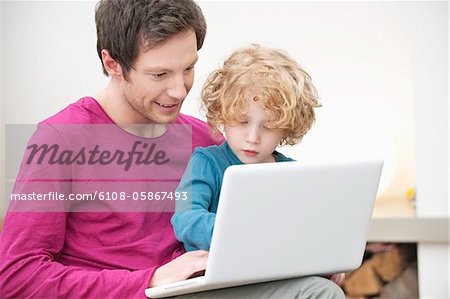 Close-up of a man assisting his son in using a laptop