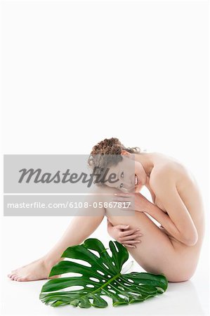 Naked woman sitting with a philodendron leaf beside her