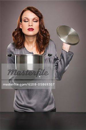 Young woman smelling aroma from stew pot