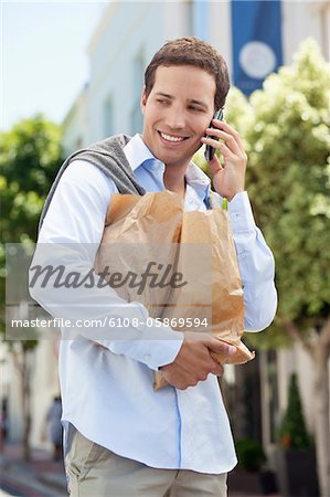 Mid adult man talking on a mobile phone with paper bags full of vegetables