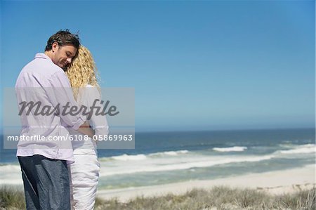 Man embracing a woman from behind on the beach