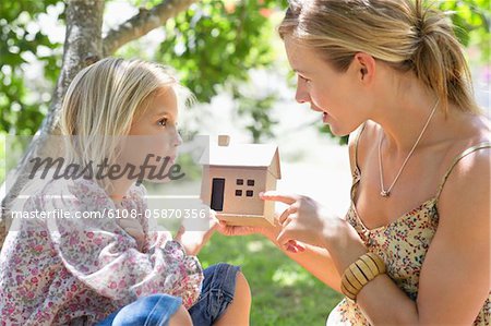 Little girl and her mother holding dollhouse outdoors