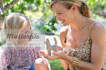 Little girl and her mother looking at toy in hand outdoors