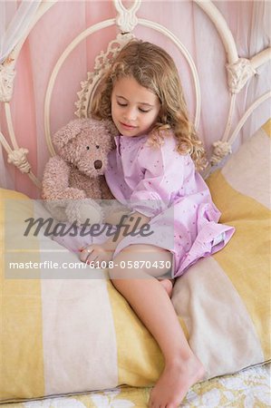 Cute little girl sitting with teddy bear on the bed