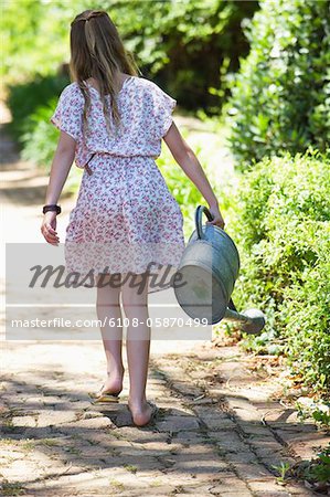 Rear view of a little girl watering to plants outdoors