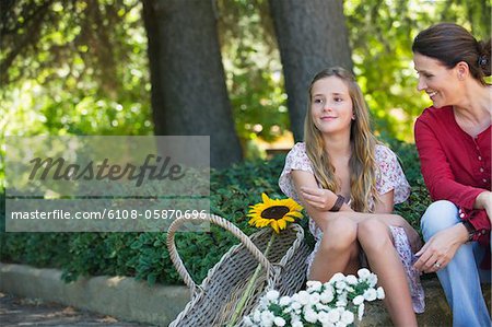 Little girl and mother sitting outdoors with flowers in the basket