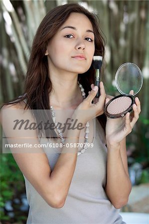 Portrait of a beautiful young woman applying make-up