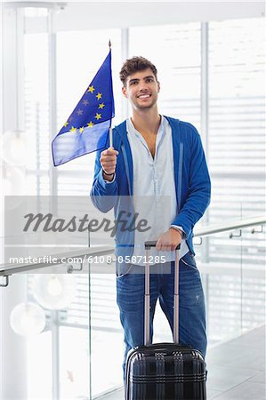 Portrait of a man holding European union flag and a suitcase at an airport