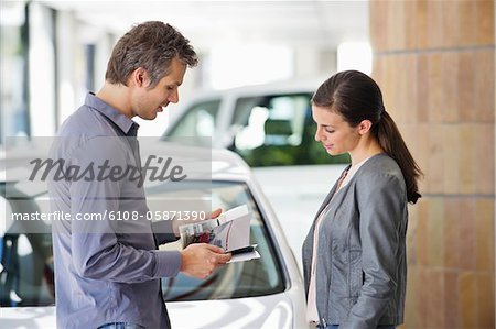 Side profile of a couple looking at catalog in car showroom