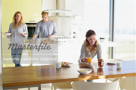 Girl putting breakfast on a dining table with her parents in the background