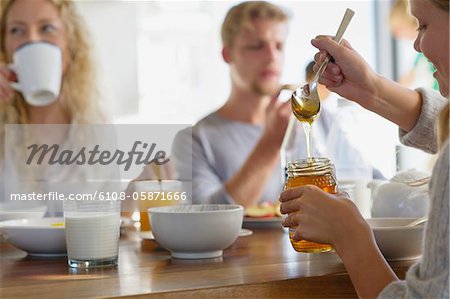 Family eating breakfast at home with focus on a girl taking out honey