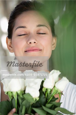 Beautiful young woman holding bunch of white flowers with her eyes closed