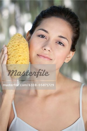 Beautiful young woman holding a bath sponge on her face