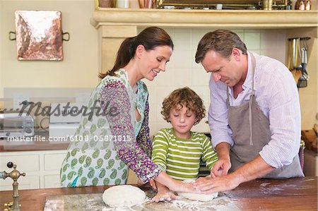 Cute little boy and his parents kneading dough at kitchen