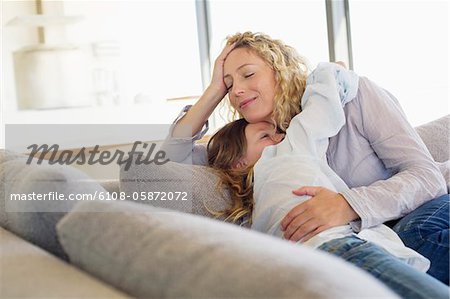 Mid adult woman and her daughter hugging each other on a couch