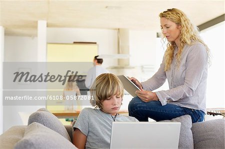 Teenage boy using a laptop and his mother using a digital tablet