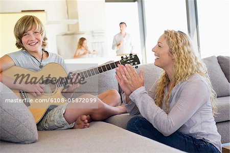 Teenage boy playing a guitar with his mother clapping