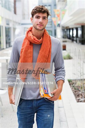 Portrait of a man walking with books and a laptop in hands