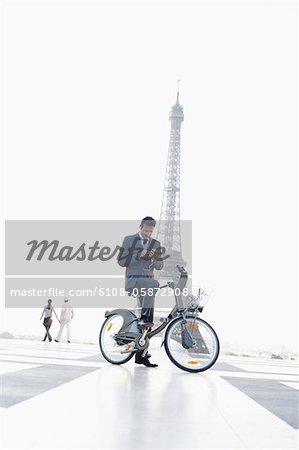 Businessman operating a mobile phone on a bicycle with the Eiffel Tower in the background, Paris, Ile-de-France, France