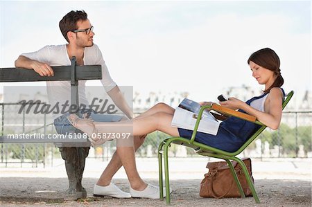 Woman using a mobile phone with a man sitting in front of her, Jardin des Tuileries, Paris, Ile-de-France, France