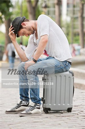 Man sitting on the suitcase at the roadside, Paris, Ile-de-France, France