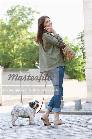 Woman holding a puppy on leash while talking on a mobile phone, Paris, Ile-de-France, France