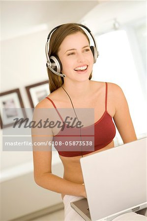 Young woman smiling, listening to music with headphones, laptop on her knees