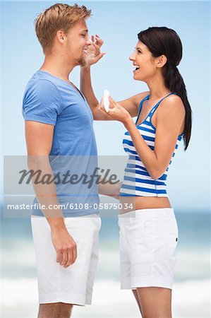Woman applying suntan lotion on man's face