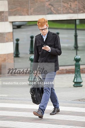 Businessman crossing a road while using a mobile phone