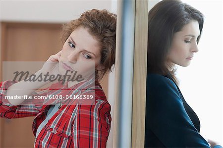 Two female friends standing back to back against a door