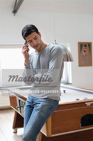 Man leaning against a pool table while talking on a mobile phone