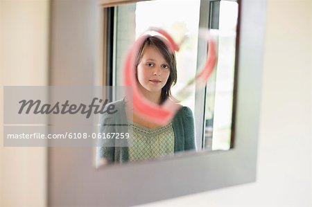 Girl looking at reflection in mirror decorated with heart shape