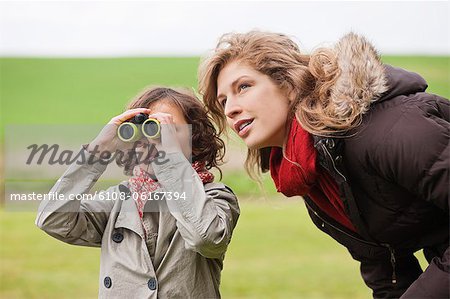 Boy looking through binoculars standing with his mother