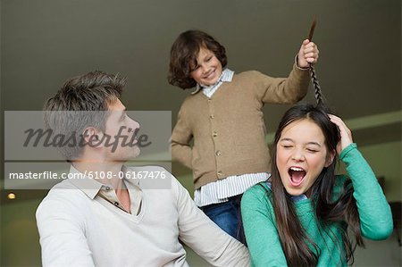 Boy pulling his sister's braid with his father looking at him