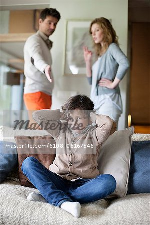 Boy covering ears with hands while his parents arguing in the background