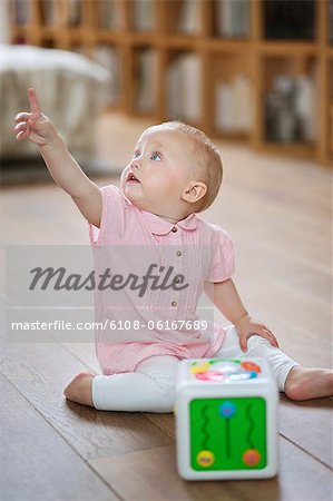 Baby girl sitting on the floor and pointing away with finger