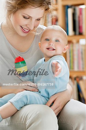 Baby girl sitting on the lap of her mother playing with a toy