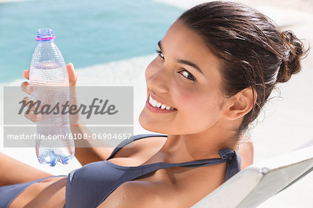 Beautiful woman holding a water bottle while sunbathing on the beach
